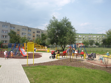duży plac zabaw otoczony trawnikami i ścieżkami, w tle bloki mieszkalne