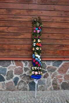 Palma wykonana przez Julię Maszerowską z kolorowymi kwiatami z bibuły i trawami, ustawiona pionowo