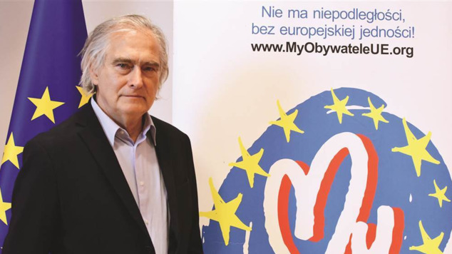starszy mężczyzna pozuje do zdjęcia na tle roll-upu z logo Fundacji My Obywatele UE