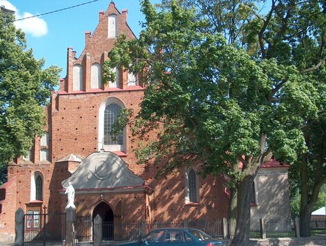 Kościół z czerwonej cegły otoczony drzewami.