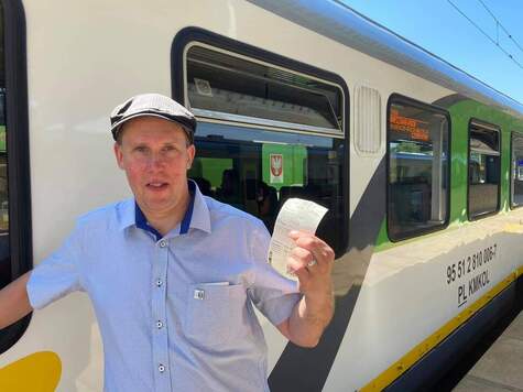 mężczyzna z biletem w dłoni pozuje do zdjęcia na tle pociągu
