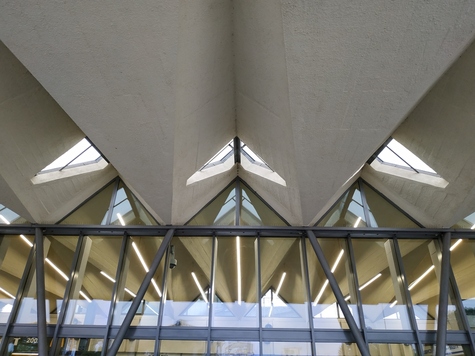 Pofalowany fragment dachu układający się w literę W wewnątrz budynku. Pod nim widać balustradę przejścia dla pasażerów
