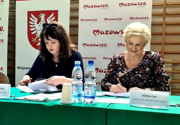 Dwie kobiety podpisują dokumenty siedząc przy stole
