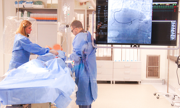 mężczyzna ubrany w niebieski farcuh medyczny stoi przy stole operacyjnym