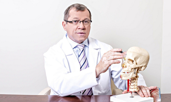 mężczyzna w białym fartuchu, siedzi przed anatomicznym modelem czaszki