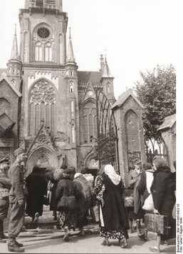 Archiwalne zdjęcie kościoła przy ul. Wolskiej w Warszawie. Przy bramie stoją niemieccy żołnierze i pilnują ludzi pędzonych do wnętrza kościoła.