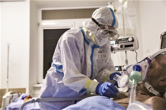 Pielęgniarz w kombinezonie poprawia respirator pacjentowi