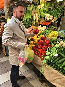 Mężczyzna w jasnej marynarce robi zakupy przy straganie warzywnym