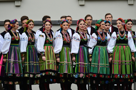 Tancerki z zespołu Mazowsze w ludowych strojach stoją w dwóch rzędach, uśmiechają się i pozują do zdjęcia