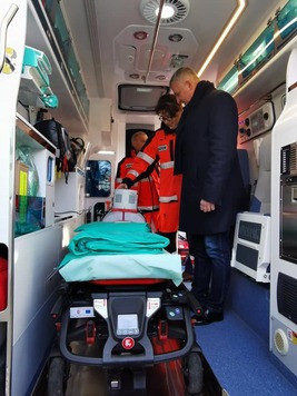 Wicemarszałek Rajkowski stoi przed noszami wewnątrz ambulansu. Ratowni, który stoi obok niego, wskazuje na nosze