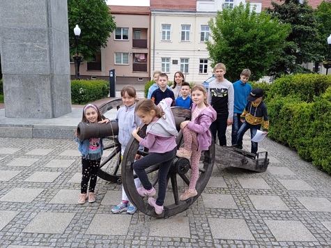 grupa dzieci stoi wokół armaty na placu miejskim