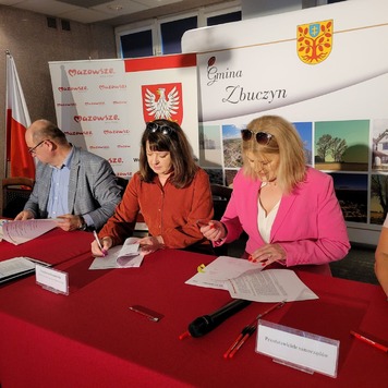 Na zdjęciu dwie kobiety i jeden mężczyzna siedzą przy stole i podpisują umowę