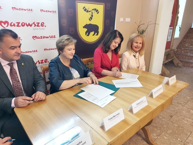 4 osoby siedzą przy stole na tle herbu Węgrowa i podpisują umowę