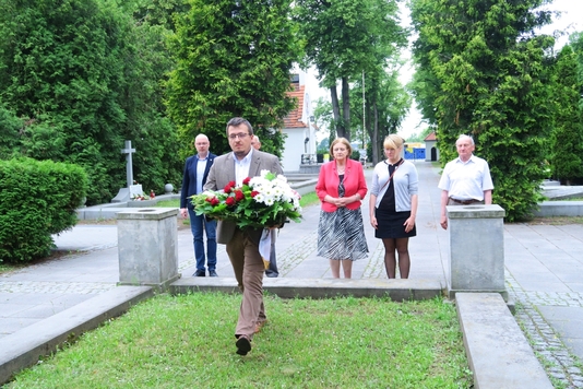 Na pierwszym planie Burmistrz Radzymina Krzysztof Chaciński składa, w imieniu komisji, wieniec przed zbiorowym grobem na Cmentarzu Żołnierzy Poległych 1920. W tle stoją członkowie komisji.