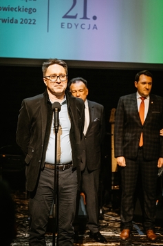 Piotr Szulkowski stoi przy mikrofonie. W tle widać wiceprzewodniczącego Marcina Podsędka.