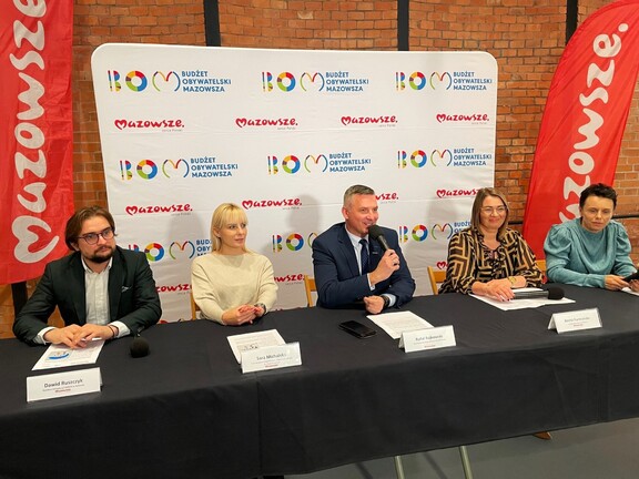 Wicemarszałek Rajkowski siedzi przy stole konferencyjnym wraz z czterema innymi przedstawicielami urzędu. Za nimi jest wielki baner z logiem BOM