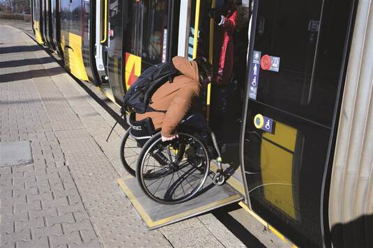 Osoba z niepełnosprawnością wjeżdża na wózku do tramwaju.