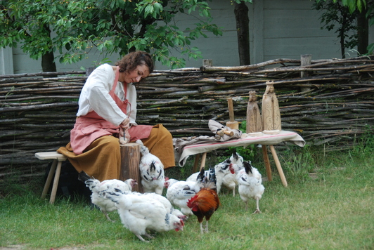 Kobieta pracująca nad rzeźbą. Wokół niej wiejskie kury