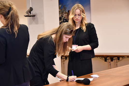 Praktykantka podpisuje dokument przy stole prowadzących spotkanie