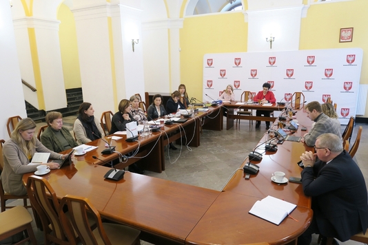 Uczestnicy posiedzenia komisji siedzą przy stole w sali konferencyjnej Sejmiku Województwa Mazowieckiego.