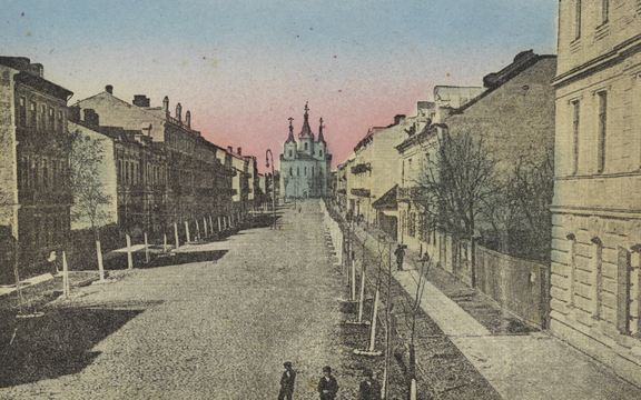 Przedwojenna, koloryzowana pocztówka prezentuje ulicę, której obie pierzeje są zabudowane kamienicami i obsadzone młodymi drzewami. Oś ulicy zamyka trójwieżowa świątynia.